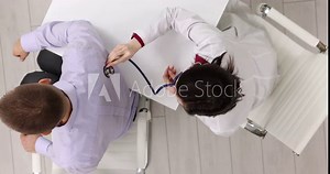 Female doctor examines male patient using stethoscope in medical office