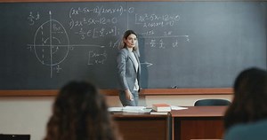 Caucasian female professor at high school writing on blackboard while explaining math for students. University knowledge. Woman teacher explaining mathematics formulas and teaching.