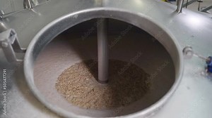Modern processing equipment is operating at the beer production plant. Automated equipment is mixing the ingredients for beer production. Stirring the barley in the beer production equipment
