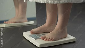 Weight problems, lady stepping on scales at home to check weight, extra fat