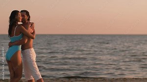 High-quality beach travel video in slow motion. Couple in love embracing, having romantic tender moments on the beach. Handsome man shirtless with a stunning tanned woman in blue bikini during summer