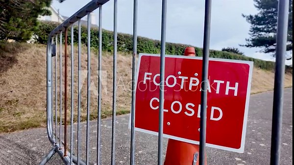 Red footpath closed sign behind a metal railing along a walkway, signaling restriction and safety.