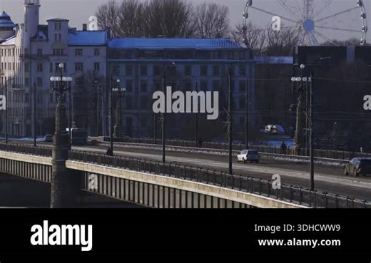 Aerial scene in Riga, Latvia shows a snow dusted bridge with ornate lamp posts, clear traffic, trams, vans, pedestrians, and a Ferris wheel on a sunny winter day Stock Video Footage - Alamy