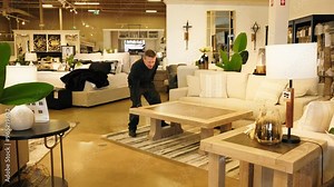 Man in black work clothes tests the weight of a coffee table in a furniture store