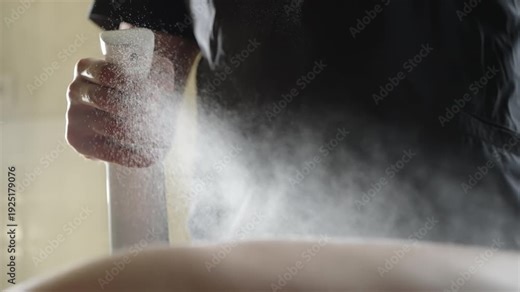 Close-up of a person using a white spray bottle to apply a fine mist over skin, capturing the aerosol cloud and trigger action during a hygiene treatment or spa application