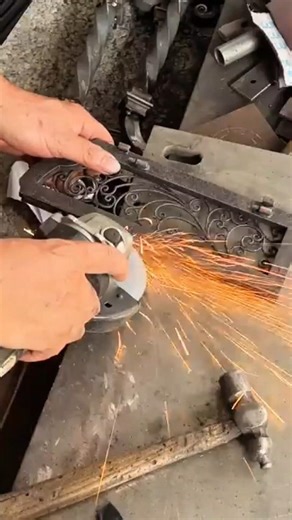 grinding a decorative black metal frame using an electric angle grinder in an indoor workshop