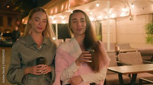Happy girlfriends walk going city street outside urban European women carefree enjoying relaxation vacations weekend evening talk together holding coffee hand friendship meet chatting cafe gen z drink