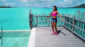 Fitness woman doing Jumping Jacks AKA Star Jumps as warm up exercise workout outside in amazing setting in Tropical paradise.