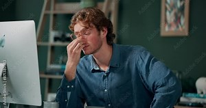 Headache, man and tired at computer with glasses, burnout or stress in modern office. Male designer, brain fog or frustrated for deadline with anxiety, depression or overwhelmed by work in creativity