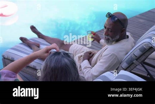 Senior couple lounging poolside, woman pointing at pink float, African American man offering toast. Pair, outdoor, vacation, leisure, deck, pool, sunshine Stock Video Footage - Alamy
