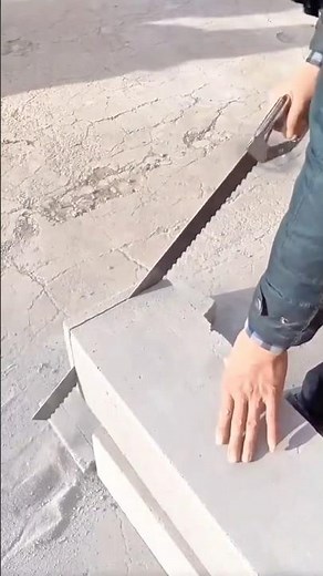 Worker cutting lightweight concrete blocks manually with a large hand saw