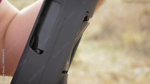 Man loading a shell into a pump action shotgun in slow motion. The young caucasian man loads the red shotgun slug into the 12 gauge semi-automatic weapon on a gun range for target practice.