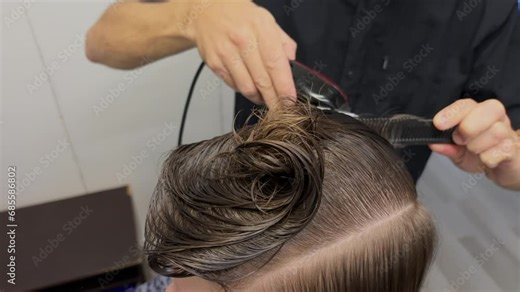 Hands of barber cutting hair of caucasian man with a trimmer and comb. Self care lifestyle. Trendy modern hairstyle in beauty salon. Hairdo. Shaves his hair with an electric razor. Wet dark hair.