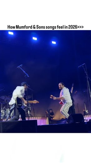 Discover Good Song | Music on Instagram: "The video captures a dynamic live concert from a low-angle, vertical perspective. A band performs energetically on a multi-level stage under vibrant blue and purple lighting, with spotlights and atmospheric smoke enhancing the mood. The lineup includes a lead guitarist in white (playing a red guitar), a second guitarist (yellow guitar), a drummer, a keyboardist in a cap, and a bassist at the rear. A large LED screen behind them displays abstract visuals—