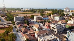 Aerial static establishing view of Banjul city cityscape and Arch 22 on sunny afternoon revealing old architecture, atlantic ocean