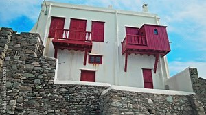 Traditional Greek whitewashed houses with red blinds and balconies in Mykonos. Beautiful properties and hotels in Mykonos, Greece.