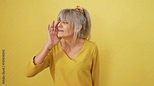 Fierce middle-aged woman with grey ponytail yelling loudly, hand amplifying her shout, epitomizing communication rage on a bright yellow background