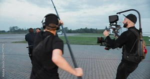 Film crew with professional equipment shooting movie outdoors. Handsome cameraman filming on set. Caucasian and African American policemen arresting male. Beautiful woman actress. Backstage concept Stock Video