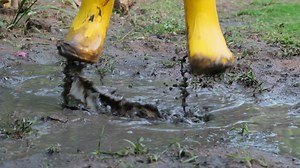 Download Close-up of the feet of a happy little girl in rubber boots jumping in a puddle. Child's feet in the muddy for free