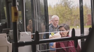 Locked-down view from inside bus of passengers getting on bus at stop on cloudy day