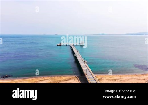 Geometric pier with a T shaped end, sandy beach in foreground, distant mountains and hazy sky. Aerial view of long concrete pier extending into calm blue sea Stock Video Footage - Alamy