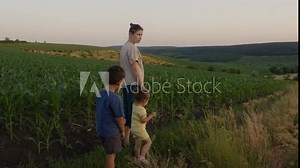 Woman in cornfield with her little daughter and son, looking at corn harvest together. Happy family, mother child walk together on corn plantation in spring.