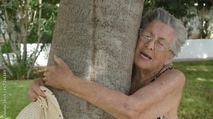 One old 90s woman hugging a tree with love for nature and closing eyes feeling the emotion inside. Happy and serene expression of aged senior lady at the park. Healthy retired people lifestyle concept Stock Video