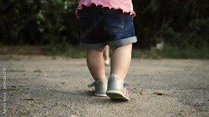A small child takes his first steps. Mom and child walk in the fresh air. The concept of children's first steps and child growing up and development. Mom and little daughter, child's feet close-up