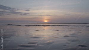 The sun is setting behind the perfect fine golden sandy beach at low tide showing tidal sand ripples.