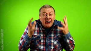 Angry mature adult Caucasian stressed man yelling, screaming and actively gesturing. Furious elderly person expressing his furious. Green background. Green screen. Close-up.