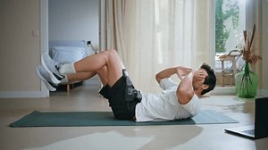 Sport man performing crunches on yoga mat at home morning workout. Active guy making bicycle exercises focusing on body strength in modern interior. Energetic athlete training endurance in apartment.