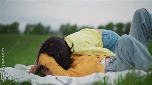 two women cuddling on blanket, tender kisses and embraces in open meadow with denim and yellow layers, overcast sky and green field, intimate romantic mood, candid closeup smiles, slow natural