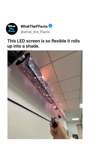 What_The_Facts on Instagram: "This video showcases an innovative, ultra-flexible rollable LED display technology that transforms a compact, ceiling-mounted roll into a massive, high-definition screen. The footage begins with a demonstrator using a remote control to trigger the motorized mechanism, which smoothly unfurls a long, thin horizontal panel that gradually expands into a large, seamless vertical display. Once fully deployed, the screen exhibits vibrant 8K underwater footage featuring a l