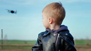 Happy boy plays with a drone in nature. Child controls the drone using a remote control.