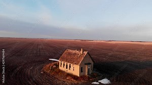 Drone backing slowly away from an isolated abandoned one-room schoolhouse. The drone slowly rises as it backs away showing the vast prairie landscape.