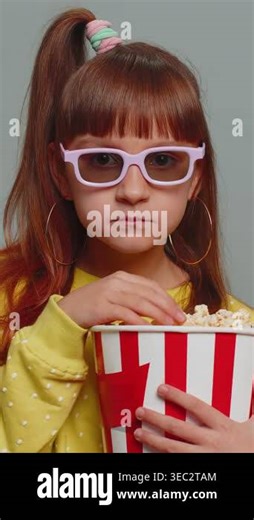 Excited young toddler girl in 3D glasses eating popcorn, watching interesting tv serial, sport game, film, online social media movie content. Teen female child kid on studio gray background. Vertical Stock Video Footage - Alamy