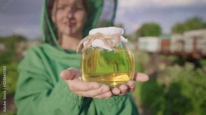Beekeeper with honey. A woman farmer shows honey from her apiary. Yellow honey in a glass jar. Liquid sweet gold. Home apiary, small business. Apiarist, hiver, beemaster. Apiculture, honeycomb
