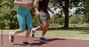 Fit sports couple running together on a race track in a lush green park, focusing on cardio and stamina exercises.