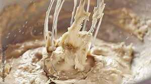 Metal whisk is mixing dough with oat flakes for baking, creating a smooth and well combined mixture. The process of preparing ingredients for a delicious baked treat
