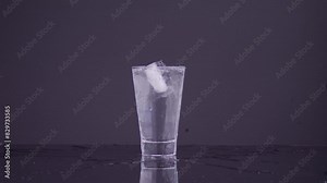 Slow-motion of ice cube falling in glass of water makes splash and water scattered out of the cup