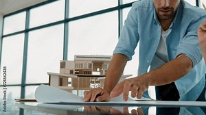 Closeup of smart architect engineer hands using project plan explain house model construction to young coworker. Professional architect pointing at project plan on table. Focus on hand. Tracery