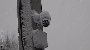 outdoor IP security camera spins rotating follow track watch on a concrete pillar with a power box and LED. Winter with snow. High quality 4k footage