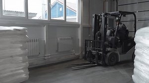 A worker in a warehouse unloads pallets with an electric forklift with sacks of flour. Adult Man works indoors on a forklift.