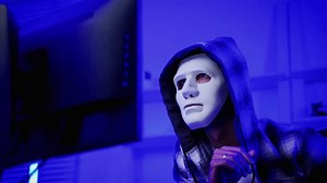 hacker wearing a white mask is using a computer to steal confidential information.Concepts: computer crime, burglary, business security on computer networks
