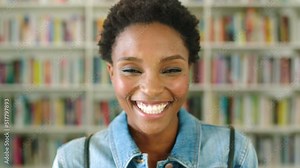 Closeup portrait of a beautiful young librarian or bookstore owner standing with a bookshelf in the background. Happy young woman working in a bookshop with reading or study material for research