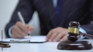 Gavel on block as jurisdictional symbol, attorney signing evidence on background