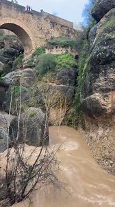 Puente Viejo (Old Bridge) in Ronda, Spain. This bridge is one of three historical bridges that cross the 120-meter-deep chasm (known as the El Tajo gorge) that divides the city of Ronda. It spans the Guadalevín River. The Puente Viejo was built in 1616 and is the second oldest and second lowest of the three bridges in the city. The image captures the view of the bridge and the river below, which appears to be experiencing high flow. | Livi Pappas Blanco
