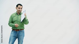 Funny young man standing holding the paper holder with word "bisiness" writen on it, showing it at the camera, pointing at it, playing, moving comically.