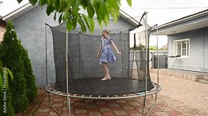 girl in blue dress and bare feet jumping on trampoline in her yard in summer Stock Video