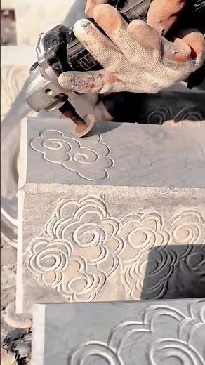The person is carving decorative swirl patterns into stone using a rotary grinding tool